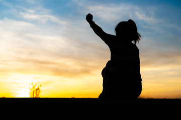 The silhouette of a woman sitting, feeling happy and raising her hand.