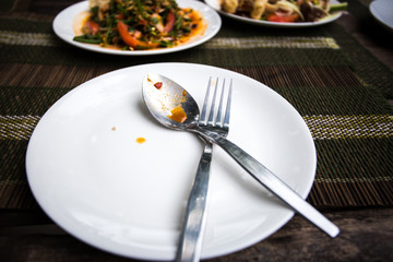 White dish and fork on wooden table. Dinner eating at restaurant