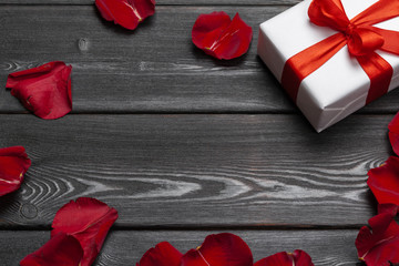 Gift box and rose petal on wooden background.