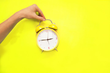 Creative flat lay concept top view of woman hand shirt holding the yellow vintage   alarm clock on...