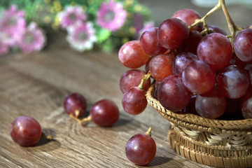 a bunch of red grapes on bamboo basket and flowers  as background