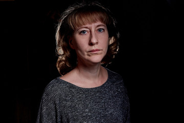 Portrait of a sad middle-aged woman in the room. Photo shoot in a dark key