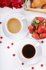 Two cups of coffee, strowberry and croissants on white table.  Festive breakfast with a bouquet of red roses. Happy Valentines day.  Top view.