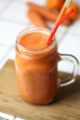 Orange healthy refreshing veggie carrot smoothie in a transparent glass with tubules on a white table by the day healthy nutrition diet detox