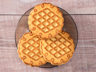 Three cookies in a saucer on a light wooden pine background