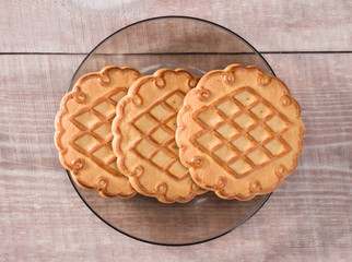 Three cookies in a saucer on a light wooden pine background