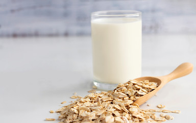 A glass of milk and oats in spoon on the white table. Its are a nutrient-rich food associated with...