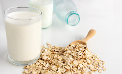 A glass of milk and oats in spoon on the white table. Its are a nutrient-rich food associated with...