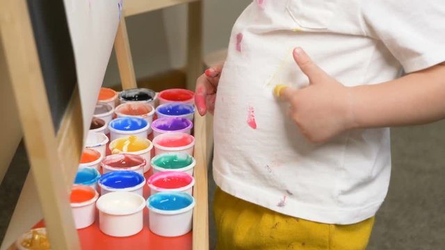Cute little boy (toddler, two years old) is painting on tee. Washable finger paints for Babies Kids, art, creative. Dirty cloth (t-shirt), washing laundry concept. 