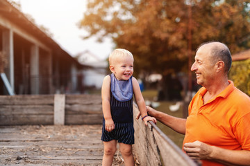 Fototapeta premium Grandfather standing next to trailer. In the trailer smiling grandson standing. Countryside exterior.