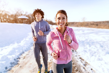 Happy Caucasian friends in sportswear running outdoors. Wintertime, snow all around. Healthy lifestyle concept.