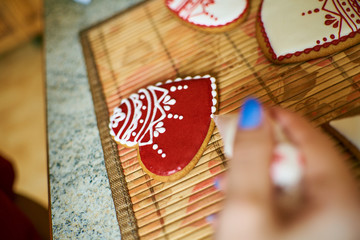 hands of a girl paint homemade heart-shaped cookies with patterns, love