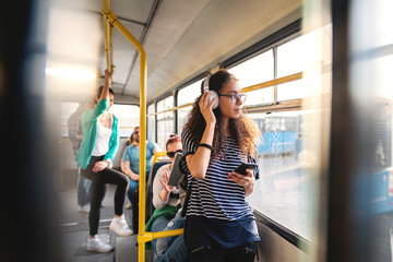 Beautiful mixed race woman listening music, using smart phone and standing in public transportation.