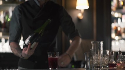 A professional bartender opens a bottle of champagne or sparkling wine while standing at the bar counter in the pub. Slow motion.