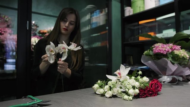 Professional woman florist works in a flower shop, cuts Orchid Cymbidium, white and red roses.