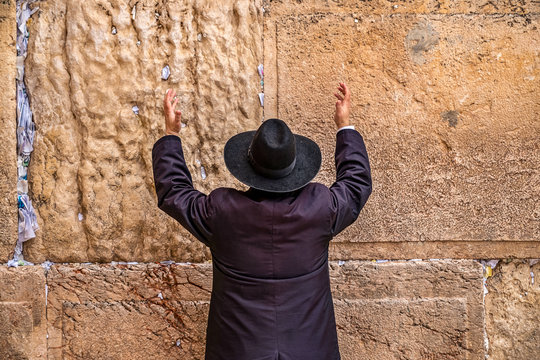 Believing Jew pray near the wall of crying in a big black hat raising his hands uphill