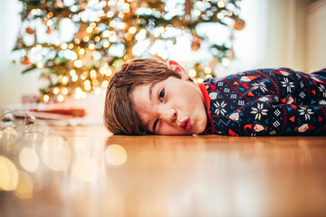 Boy lying on the floor in front of a Christmas tree pulling funny faces