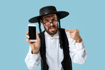 Portrait of a young orthodox Hasdim Jewish man with mobile phone at Jewish festival of Purim at studio. The purim, jewish, festival, holiday, celebration, judaism, pastry, tradition, cookie, religion