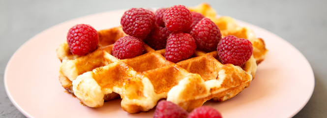 Traditional belgian waffle with raspberries on pink plate over gray background, side view. Close-up.