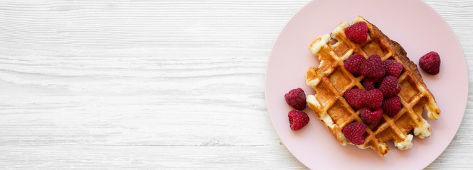 Traditional belgian waffle with raspberries on pink plate on white wooden background, top view. Flat lay, overhead, from above. Space for text.