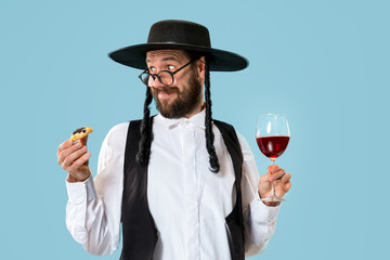 Fototapeta premium The young orthodox Jewish man with black hat with Hamantaschen cookies for Jewish festival of Purim at studio. The purim, jewish, festival, holiday, celebration, judaism, pastry, tradition, cookie