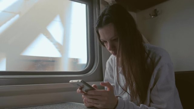 Tired young woman in train looking in mobile phone.