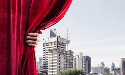Modern business cityscape behind curtain opened by businessman hand