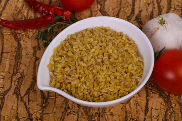 Raw bulgur in the bowl with tomatoes and garlic