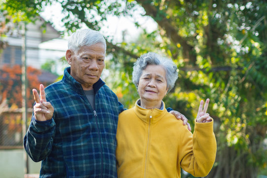 Portrait of romantic elderly man with his wife and showing victory gesture with fingers. at home garden.