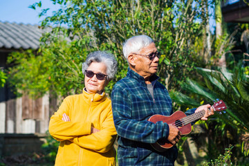 Portrait of romantic elderly man playing ukulele with his wife at home garden.