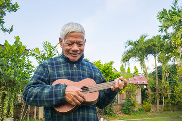 Portrait of elderly man playing ukulele in her garden.