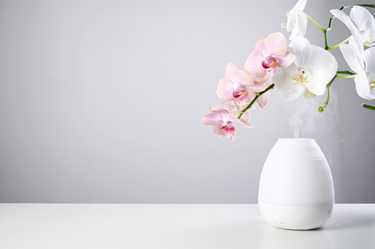 Ultrasonic Oil Diffuser And Orchid Flowers On White Table Of Gray Background