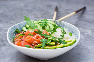 Salmon poke with avocado,  arugula and cucumber in a bowl and chopsticks