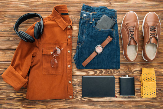 Flat lay with headphones, hip flask and male clothes on wooden background