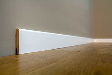 Wooden or plastic white floor plinth installation in big empty room on wooden floor and white...