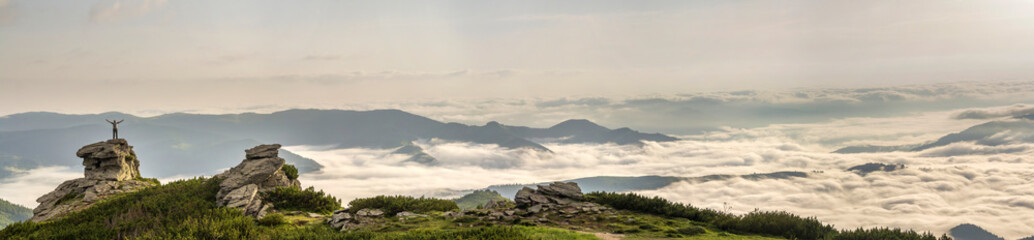 Small silhouette of tourist with raised arms on rocky formation on mountain valley filled with...