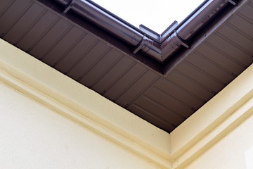 Close-up detail of cottage house corner with brown metal planks siding and roof with steel gutter...