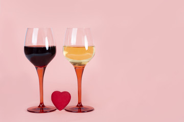 Two wine glasses with white and red wines with heart between them on pink background