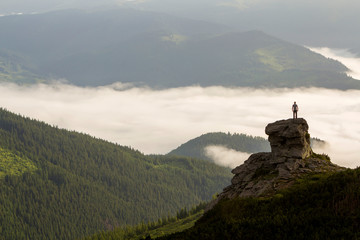Silhouette of athletic climber tourist on high rocky formation on mountain valley filled with white...