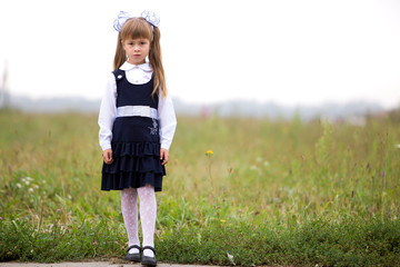 Full-length portrait of cute adorable serious thoughtful first grader girl in school uniform and...