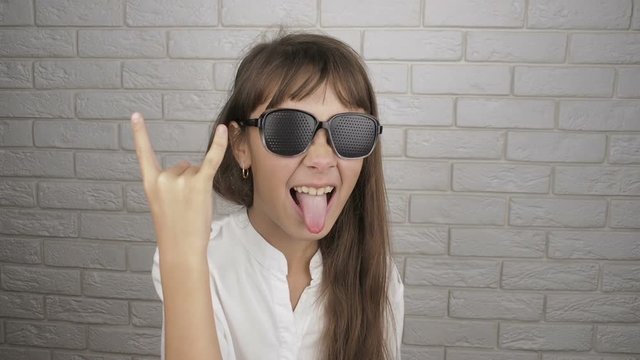 Child wearing pinhole glasses shows gesture. The girl in the obscura glasses shows her tongue.