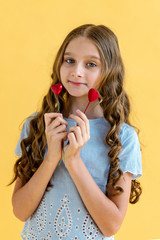 Beautiful young girl with two hearts in her hands. The concept of Valentine's day. Yellow background.