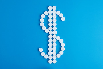 Pills in the form of dollar sign on blue background. Flat lay.