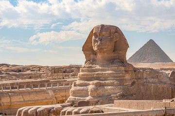 Sphinx monument against the background of large pyramids on a sunny day - obrazy, fototapety, plakaty