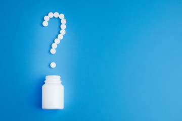 A question mark, laid out of pills and a white plastic bottle on a blue background. Medical concept.