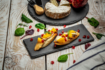 Tasty bruschetta with mango, Camembert cheese and pomegranate served on a shale board, rustic wooden table. Top view