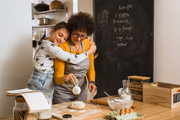 girl hugging her grandmother while baking together in kitchen
