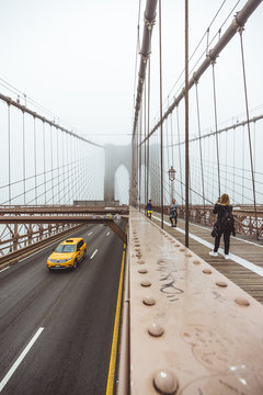 Brooklyn Bridge view on the road, taxi cars crossing the bridge. People taking pictures