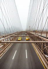 Fototapeta na wymiar Brooklyn Bridge view on the road, taxi cars crossing the bridge. Symmetrical lines