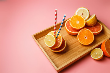 cut in half juicy citruses on a pink background on a tray next to a glass of fresh tasty juice